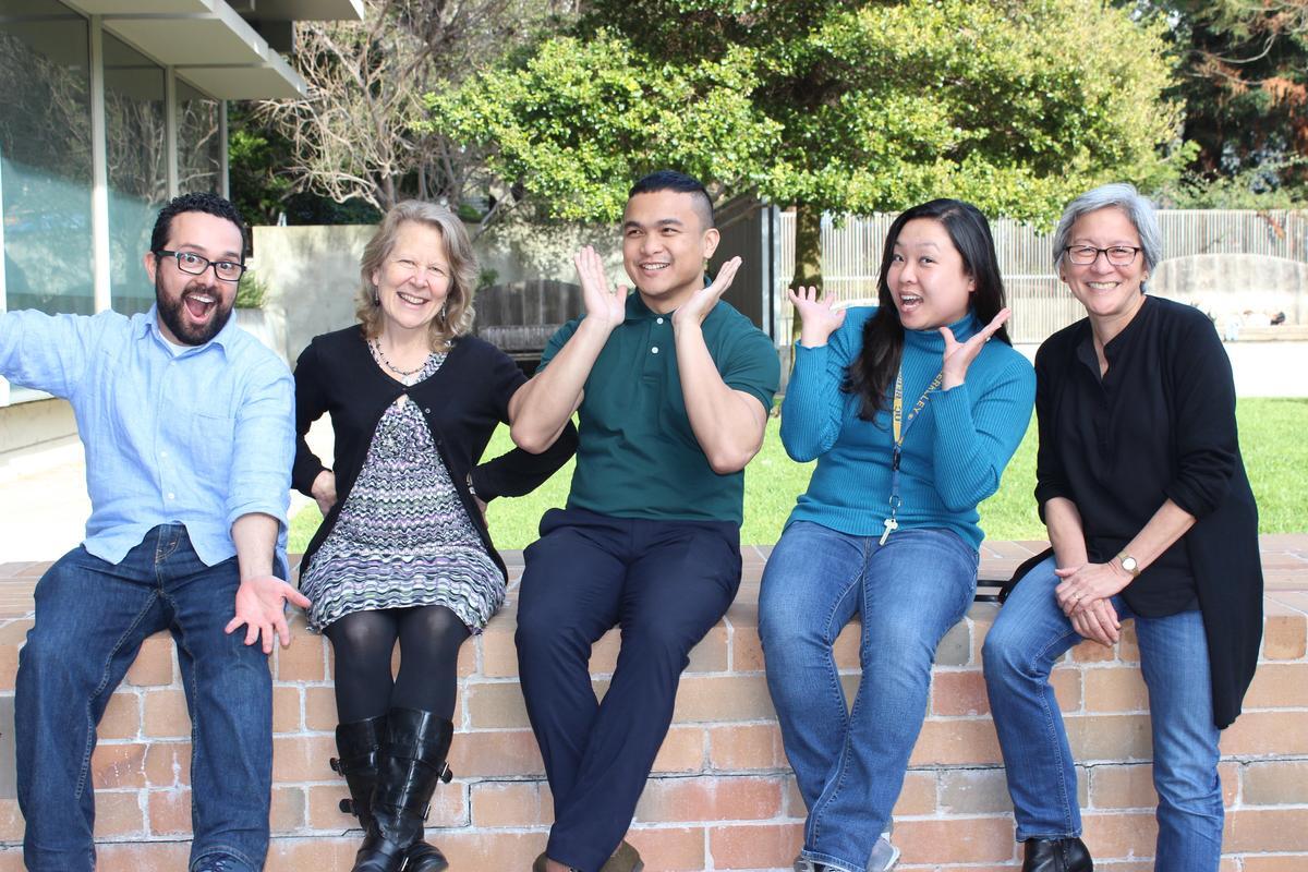 Group of people sitting on a ledge with laughing and smiling expressions.