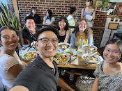 Group photo of six people sitting around a table laden with food - everyone is smiling.