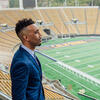 Picture of a person in a suit jacket with dark hair looking away from the camera in the Cal football stadium.