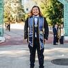 Photo of a person with long hair standing in front of Sather Gate with graduate sash.