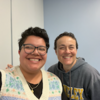 Photo of two smiling people in front of a lightly colored wall.