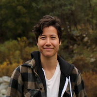 Headshot of smiling person with short dark hair in front of a natural setting.