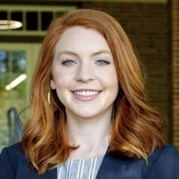 Headshot of a smiling person with shoulder-length red hair.